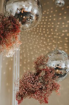 two disco balls hanging from the ceiling with red flowers in front of them and some mirrors on the wall