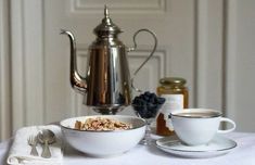 a table topped with bowls and cups filled with cereal next to a silver tea pot