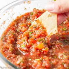 a hand dipping a tortilla chip into a bowl full of salsa and cheese