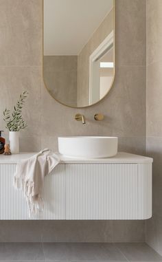 a white sink sitting under a large mirror next to a wall mounted faucet