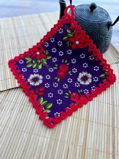 a tea pot on a bamboo mat with a red and blue flowered doily