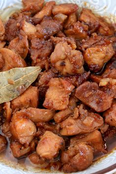 a white bowl filled with meat and sauce on top of a wooden table next to a metal spoon