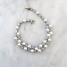 Classy and elegant, this delicate bracelet will add a touch of sophistication to any wedding gown or formal ensemble. It is featuring iridescent pearls and intricately faceted clear cubic zirconia that capture the light from every angle, sparkling beautifully. The bracelets are gold / rhodium plated for a flawless finish which perfectly enhances the intricate detailing and conveys a modern take on old elegance. Length: 7.5" (approx. 19cm); Width: and 0.4" (approx. 1cm); Weight: 7.3g. Closure is Elegant Cubic Zirconia Jewelry For Mother Of The Bride, Elegant Bridal Necklace With Pearl Chain And Crystal, Elegant Crystal Jewelry With Pearl Charm, Delicate Cubic Zirconia Bracelet For Party, Elegant Bridal Jewelry With Cubic Zirconia, Elegant White Diamond Bracelet With Sparkling Stones, Elegant Silver Crystal Bracelet With Pearl Charm, Elegant Crystal Embellished Jewelry With Cubic Zirconia, Elegant Crystal Jewelry With Pearl Chain