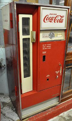 an old fashioned coca cola machine sitting on the side of a building next to a window