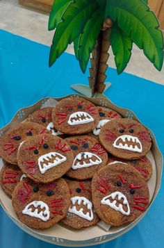 cookies decorated like monster faces on a platter with a palm tree in the background