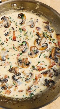 a pan filled with mushrooms and sauce on top of a wooden table