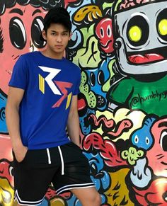 a young man standing in front of a wall covered with cartoon character images and graffiti