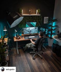 a man sitting in front of a computer on top of a wooden desk next to a plant