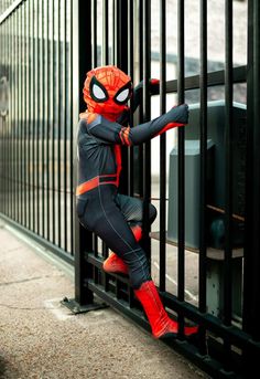 a person in a spiderman costume is leaning against a fence