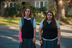 two young women standing next to each other on the side of a road with trees in the background