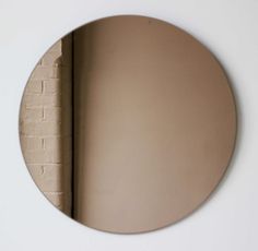 a round mirror mounted to the side of a white brick wall next to a window