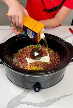 a person pouring sauce into a crock pot filled with rice and other food items