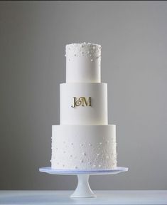 a three tiered white wedding cake with the initials j and m on each layer