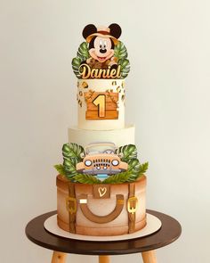 a three tiered cake with mickey mouse on top and luggage in the shape of a suitcase