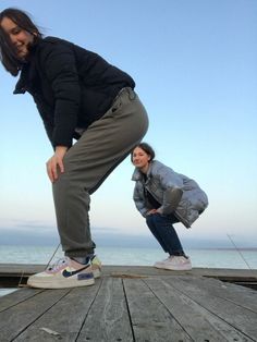 two women are standing on a dock by the water with their feet in the air