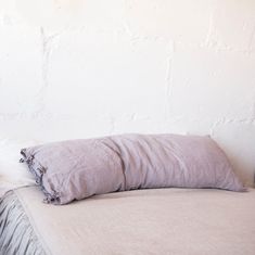 a bed with two pillows on top of it next to a lamp and a wall