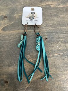 the turquoise tasseled earrings are hanging from hooks on a wooden table with a tag