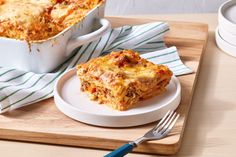 a white plate topped with lasagna next to a casserole dish on top of a wooden cutting board