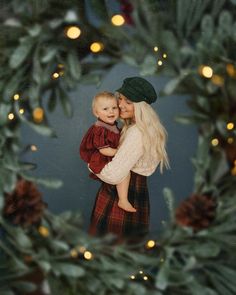 a woman holding a baby in front of a christmas wreath with lights on the background