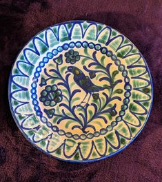 a blue and green plate with a bird on it's side sitting on a purple surface