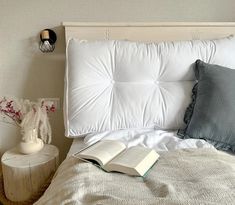 an open book sitting on top of a bed next to pillows