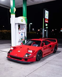 a red sports car parked in front of a gas station pump at night with its lights on