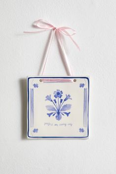 a blue and white tile hanging on a wall with a pink ribbon attached to it