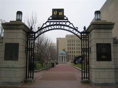 an iron gate with a clock on the top is in front of a large building