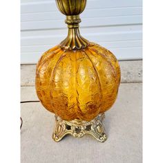 an old fashioned yellow glass vase sitting on top of a metal stand in front of a garage