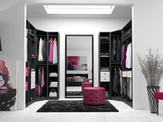 an open closet with clothes and other items in it, along with a pink ottoman