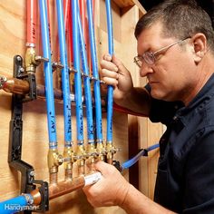 a man is working on pipes in a wooden cabinet with blue hoses attached to them