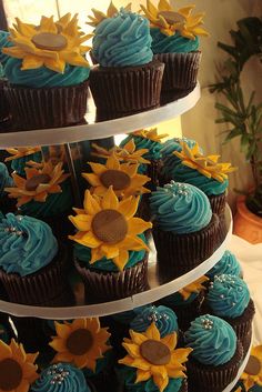 a three tiered cake with sunflowers on the top and blue frosting