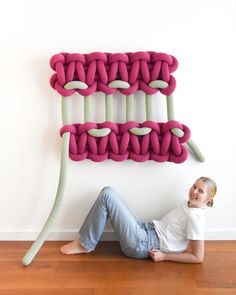 a woman laying on the floor in front of a wall sculpture made out of yarn