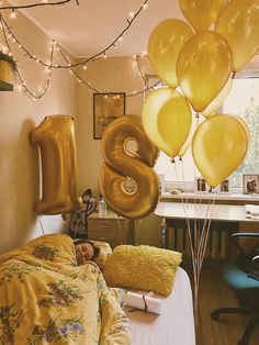 balloons are floating in the air above a bed with yellow sheets and pillows on it