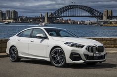 a white car parked in front of a body of water with a bridge in the background