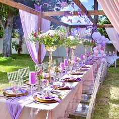 a long table set with purple and white decorations, candles, plates and flowers in vases