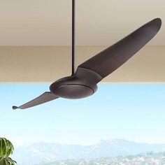 a black ceiling fan hanging from the ceiling in a room with mountains and blue sky