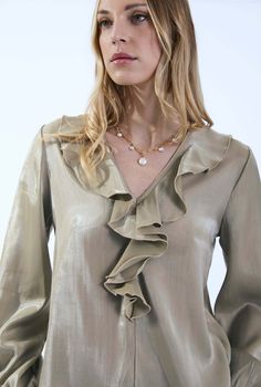 Crafted from a lightweight and flowy satin, this James Lakeland blouse exudes elegance. The luxurious sheen adds a touch of sophistication, making it ideal for various occasions. The V-neck features dramatic ruffling, creating a focal point that draws attention to the neckline. It’s a statement detail that elevates the overall design. The two long bell sleeves add a romantic flair. They end in elasticated cuffs, allowing for comfort and ease of movement. The slight ruching at the shoulders adds Elegant V-neck Ruffled Blouse, Formal V-neck Blouse With Ruffles, Elegant Ruffled V-neck Blouse, Elegant V-neck Ruffle Blouse, Gold V-neck Blouse For Work, Elegant Gold Silk Blouse, Elegant Gold Blouse For Workwear, Elegant Gold Blouse For Work, Elegant Gold Satin Blouse