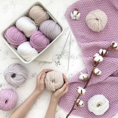 two hands holding balls of yarn next to a basket of cotton and some cotton buds