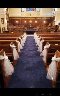 rows of pews with white tulle bows on them in an empty church aisle