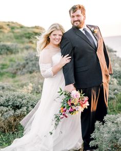 a bride and groom posing for a photo on the side of a hill by the ocean