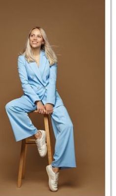 a woman sitting on top of a wooden chair wearing a blue suit and white sneakers