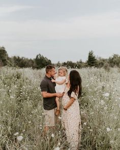 a man and woman holding a baby while standing in a field full of tall grass