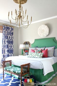 a bedroom with a green headboard, blue and white bedding, and a chandelier