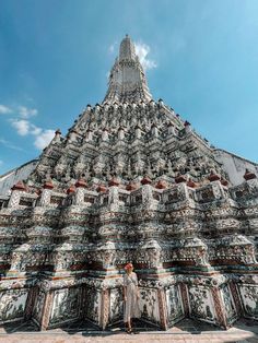 a person standing in front of a very tall building with many carvings on it's sides