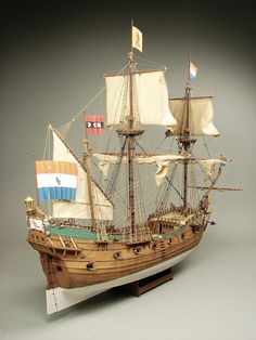 a wooden model ship with sails and flags on it's mast, in front of a gray background