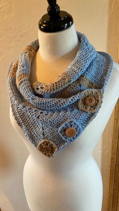 a white mannequin wearing a blue crocheted scarf with buttons on it