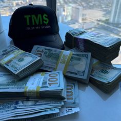 stacks of money sitting on top of a table next to a baseball cap and window