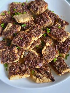 a white plate topped with pieces of meat covered in sauce and garnished with green onions