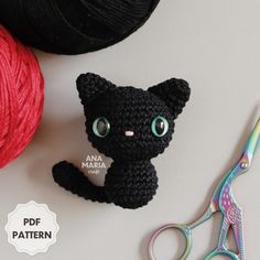 a crocheted black cat sitting next to a pair of scissors and ball of yarn